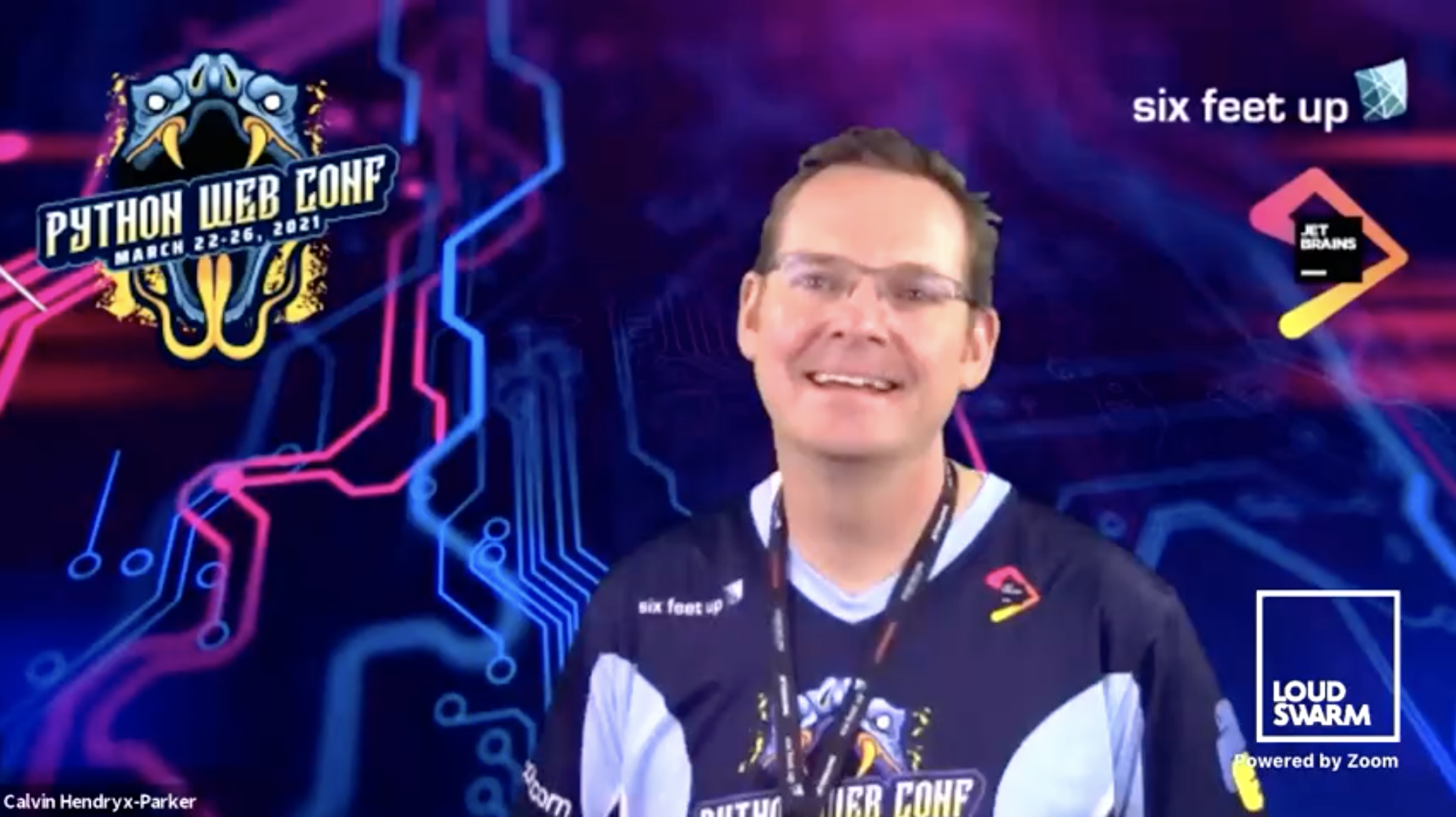 Screenshot of conference stream with a smiling man with a pink and blue virtual background